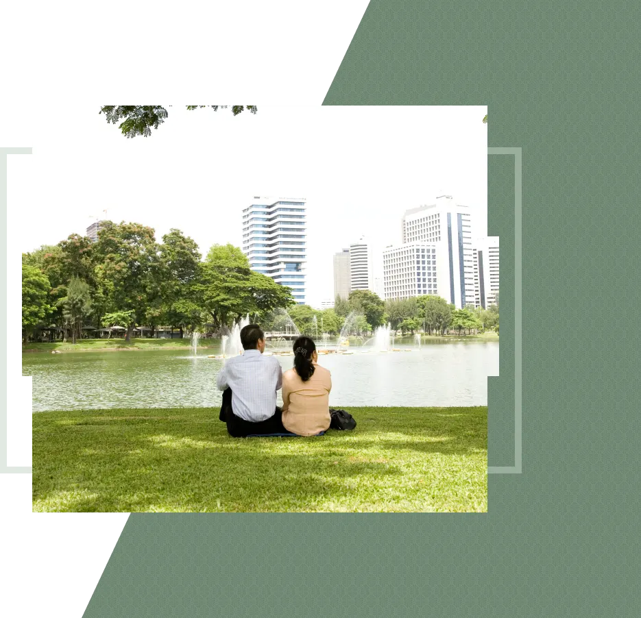 A couple sits on grass, looking at a city skyline