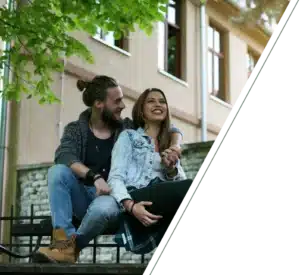 A smiling couple sits close together on a bench, holding hands