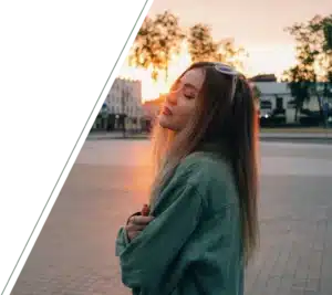 A young woman with closed eyes is lit by the setting sun