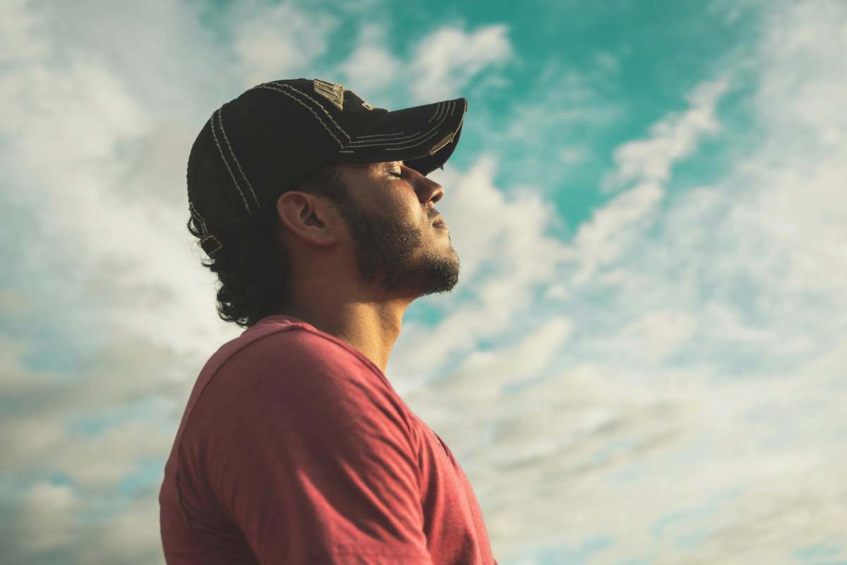 Man with eyes closed practicing 4-7-8 deep breathing under a blue sky to calm a racing mind and anxiety.