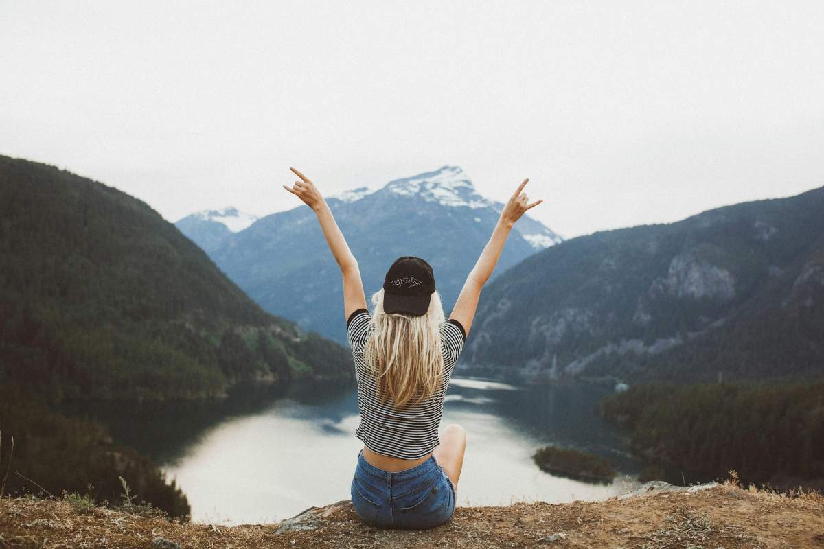 Person sitting on mountain edge with arms raised, symbolizing hope and recovery from depression.