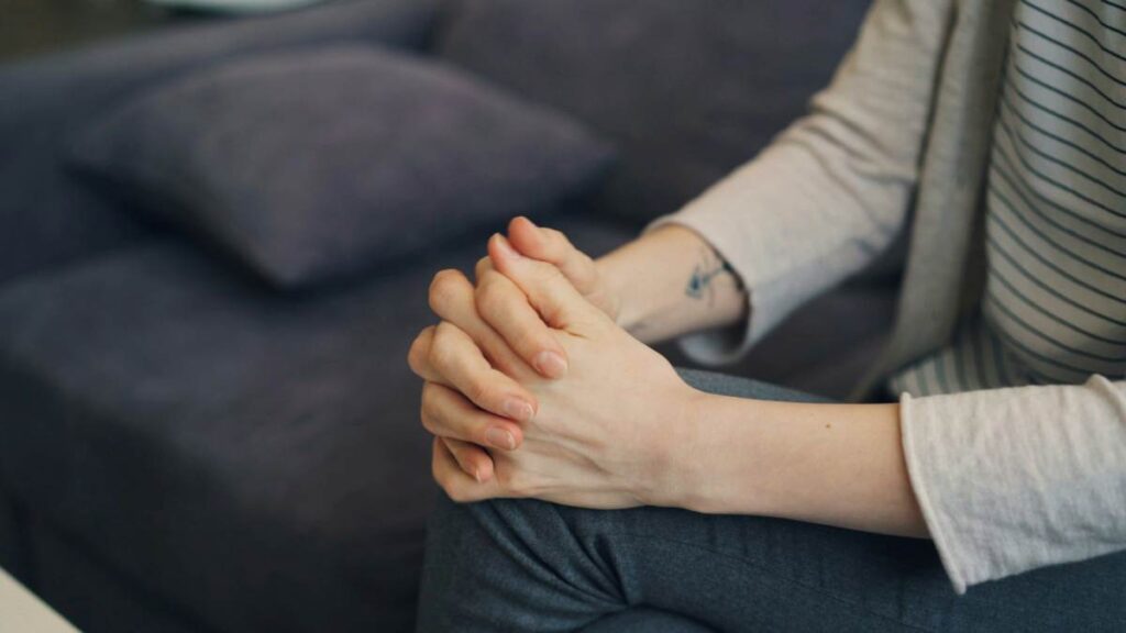 Close-up of clasped hands on a lap during counseling, showing nerves and readiness to talk.