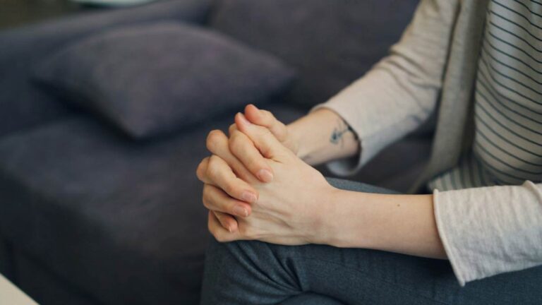Close-up of clasped hands on a lap during counseling, showing nerves and readiness to talk.