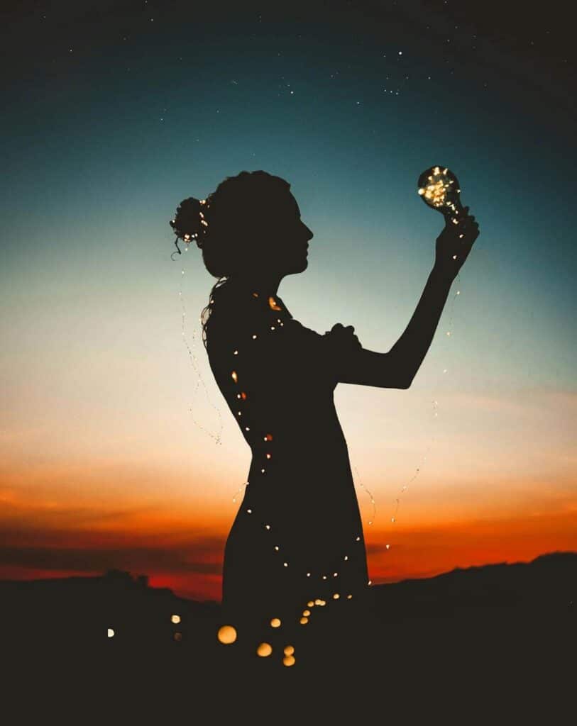 Silhouette of a woman holding glowing lights at sunset, symbolizing the mental and physical impact of workplace stress.