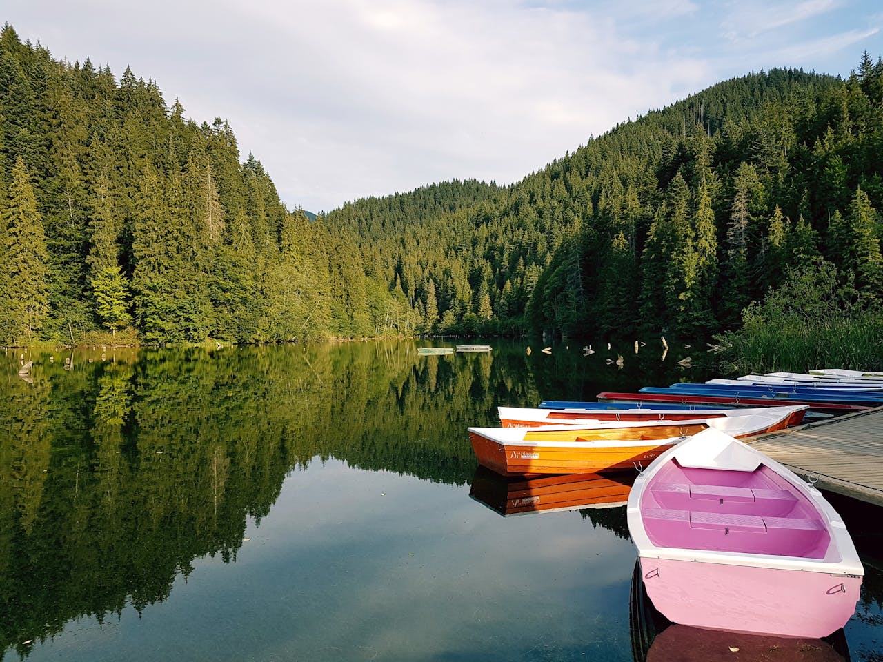 Colorful rowboats on a calm forest lake reflecting trees and mountains