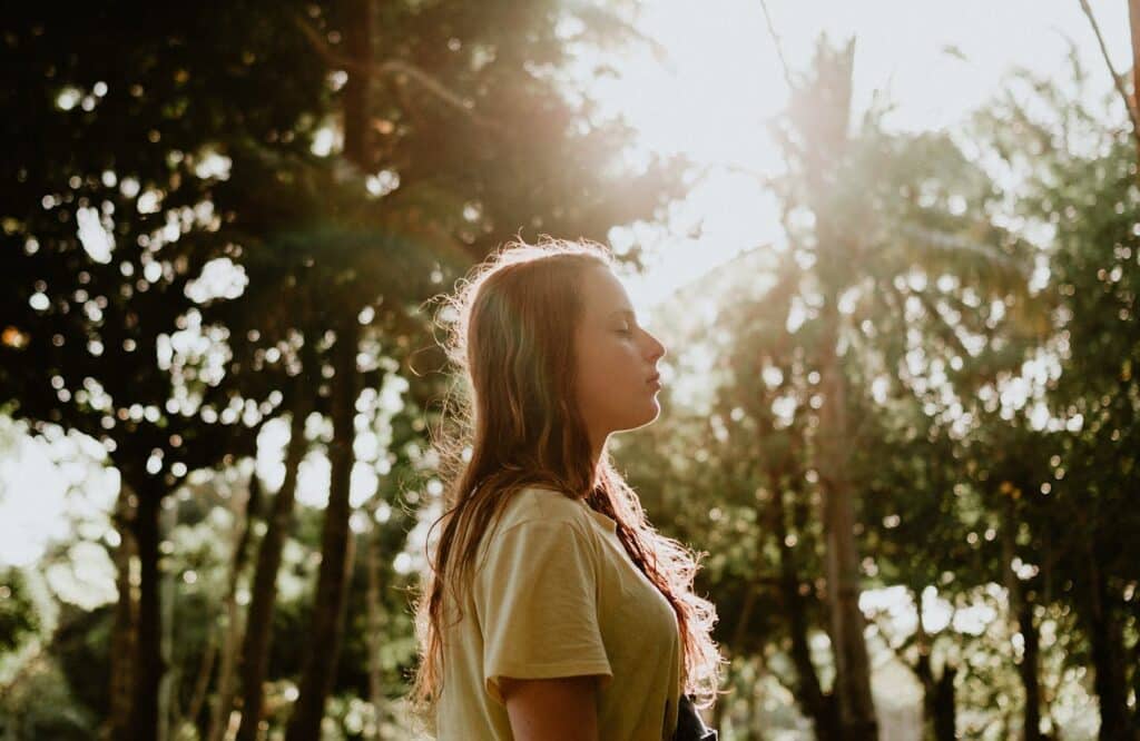 A woman standing outdoors with her eyes closed, practicing mindfulness during substance abuse recovery.