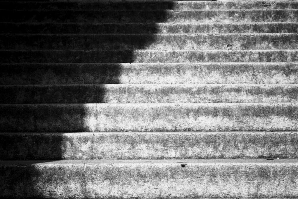 Staircase fading from shadow into light, representing the nonlinear healing journey through the stages of grief.