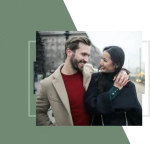 A couple standing close with city buildings behind them, smiling warmly while looking at each other