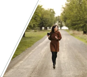 A woman running down a tree-lined street holding a camera, smiling as she looks to the side in motion