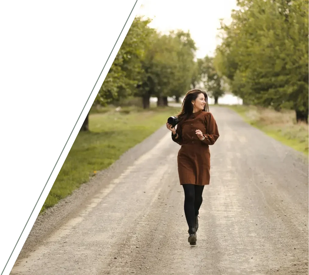  Woman walking with camera along tree lined road smiling representing freedom exploration and positive life changes