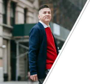 Man in formal attire standing before blurred city buildings, with a slight smile conveying confidence and calm