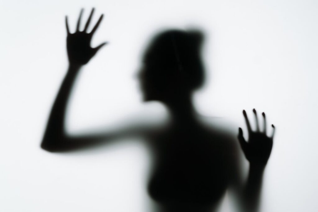 Blurred silhouette behind glass illustrating the psychological isolation associated with addiction and substance use.