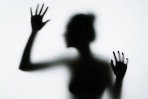 Blurred silhouette behind glass illustrating the psychological isolation associated with addiction and substance use.