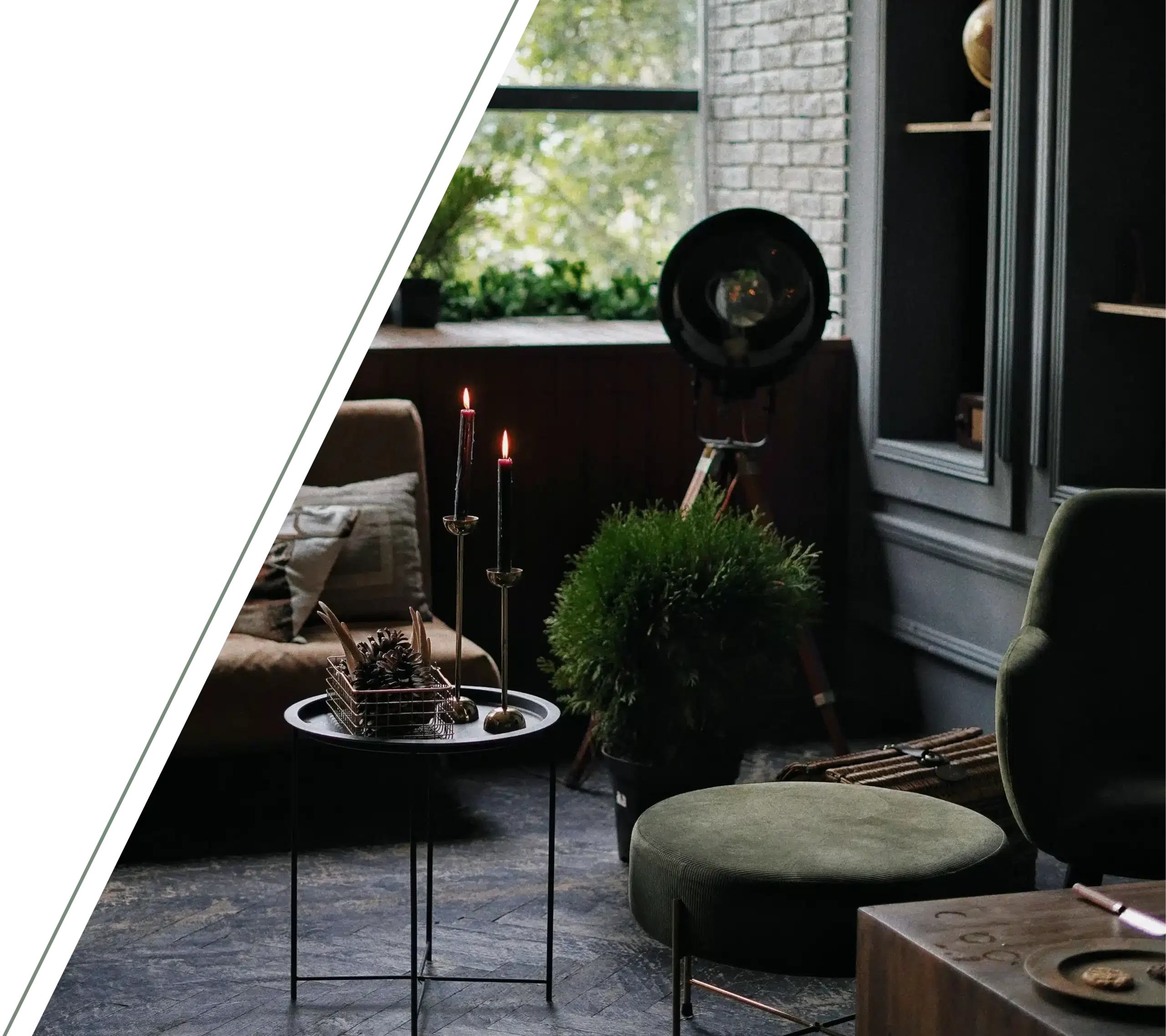 A dimly lit living room with two lit candles on a small metal table and green velvet furniture.