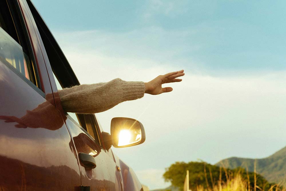 Person reaching out of a car window with an outstretched hand.