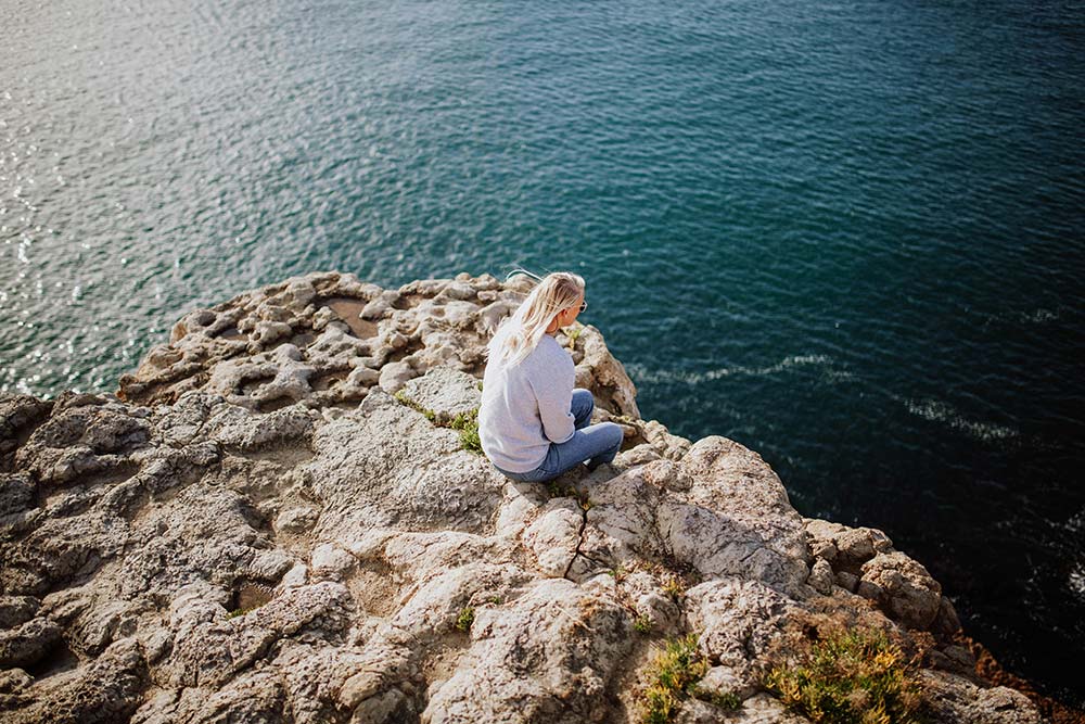A woman sitting on a rock beside the ocean.